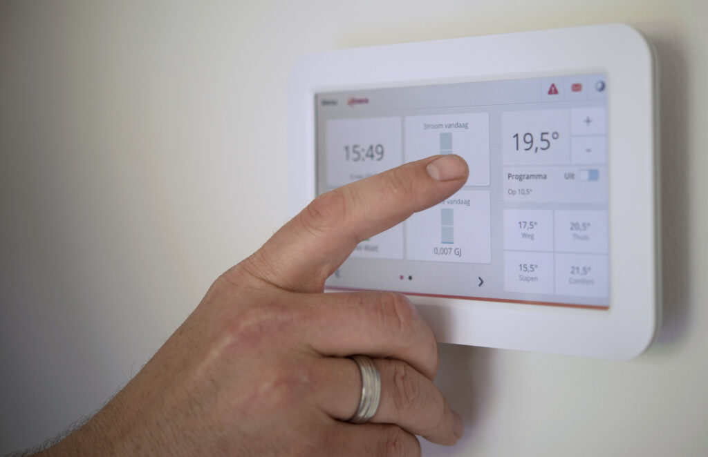 Hand berührt Touchscreen-Thermostat an Wand, Display zeigt Temperatur 19,5° und Steuerungsfelder.
