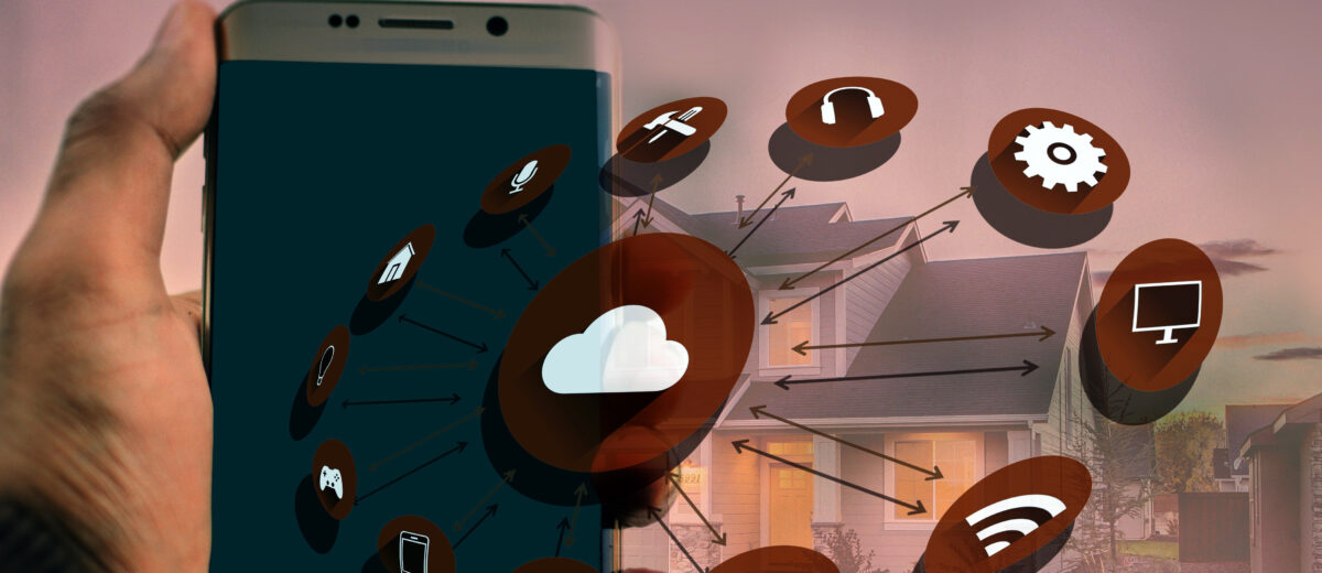 Hand hält Smartphone, überlagert mit Cloud- und Smart‑Home-Symbolen, Pfeile verbinden Geräteikonen vor einem Wohnhaus im Hintergrund