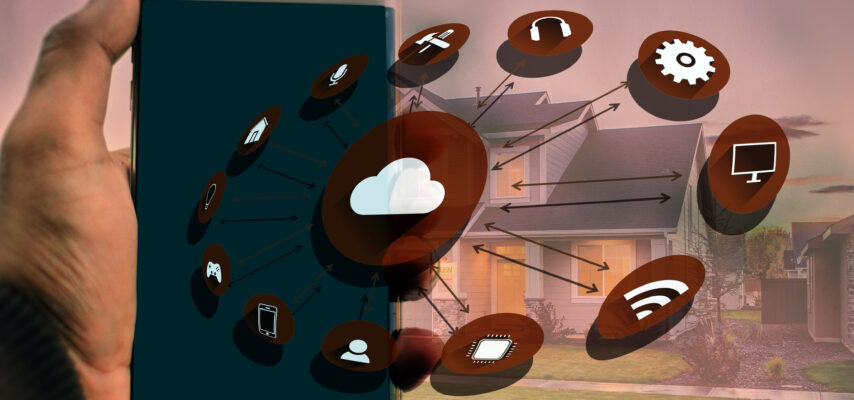 Hand hält Smartphone, überlagert mit Cloud- und Smart‑Home-Symbolen, Pfeile verbinden Geräteikonen vor einem Wohnhaus im Hintergrund
