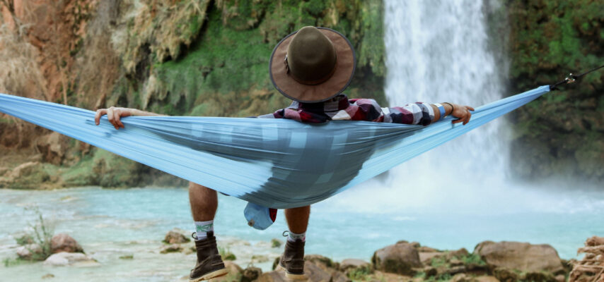 Mann liegt auf einer Hängematte vor einem Wasserfall