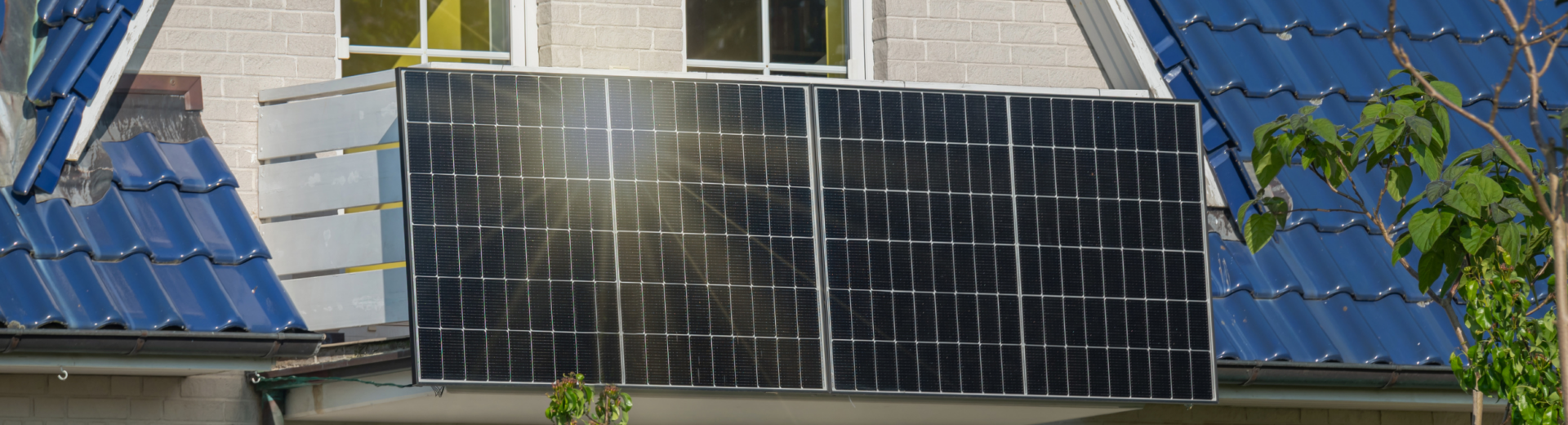 Hausgiebel mit zwei weißen Fenstern, blauer Ziegel­dachverkleidung und mehreren großen montierten Solarpanelen.