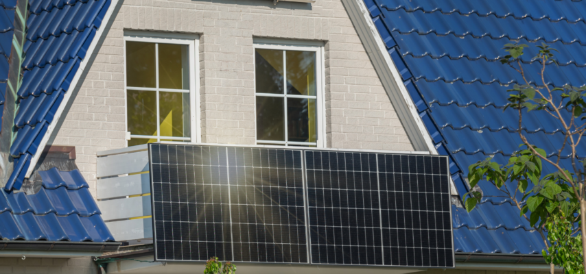 Hausgiebel mit zwei weißen Fenstern, blauer Ziegel­dachverkleidung und mehreren großen montierten Solarpanelen.