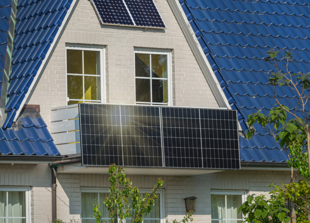 Hausgiebel mit zwei weißen Fenstern, blauer Ziegel­dachverkleidung und mehreren großen montierten Solarpanelen.