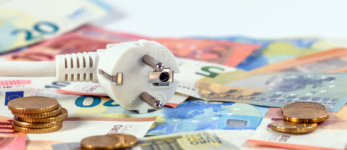 Weißer Euro-Stecker liegt auf verstreuten Euro-Scheinen und Münzen und symbolisiert Energiekosten.