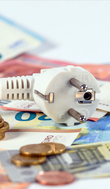 Weißer Euro-Stecker liegt auf verstreuten Euro-Scheinen und Münzen und symbolisiert Energiekosten.