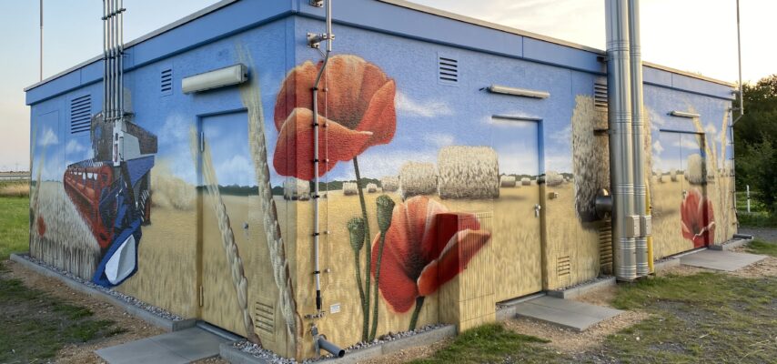 Versorgungsgebäude mit großflächigem Wandbild eines Weizenfelds mit Strohballen, roten Mohnblumen und Mähdrescher.