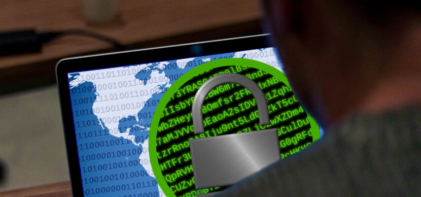 Laptopbildschirm mit Weltkarte, Binärcode und großem Vorhängeschloss-Symbol vor grünem Codehintergrund, Person im Vordergrund.