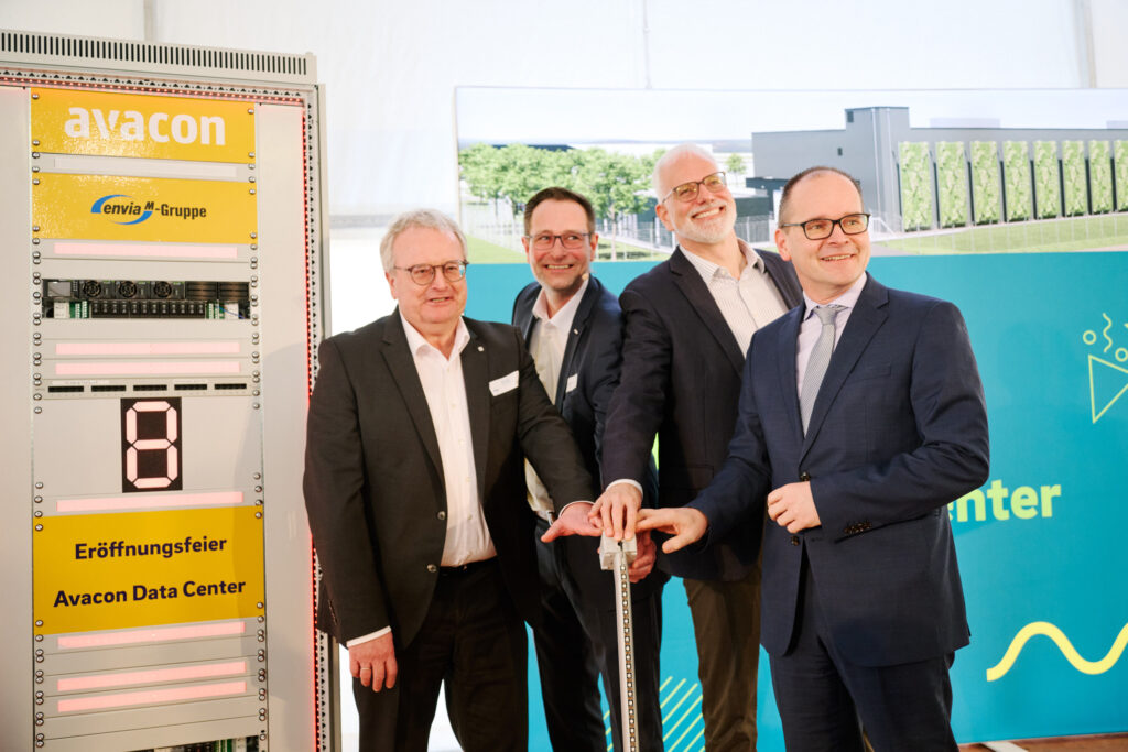 Vier Männer in Anzügen lächeln und drücken gemeinsam einen großen Knopf bei der Eröffnung eines Avacon Data Center, links ein gelbes Avacon-Display.