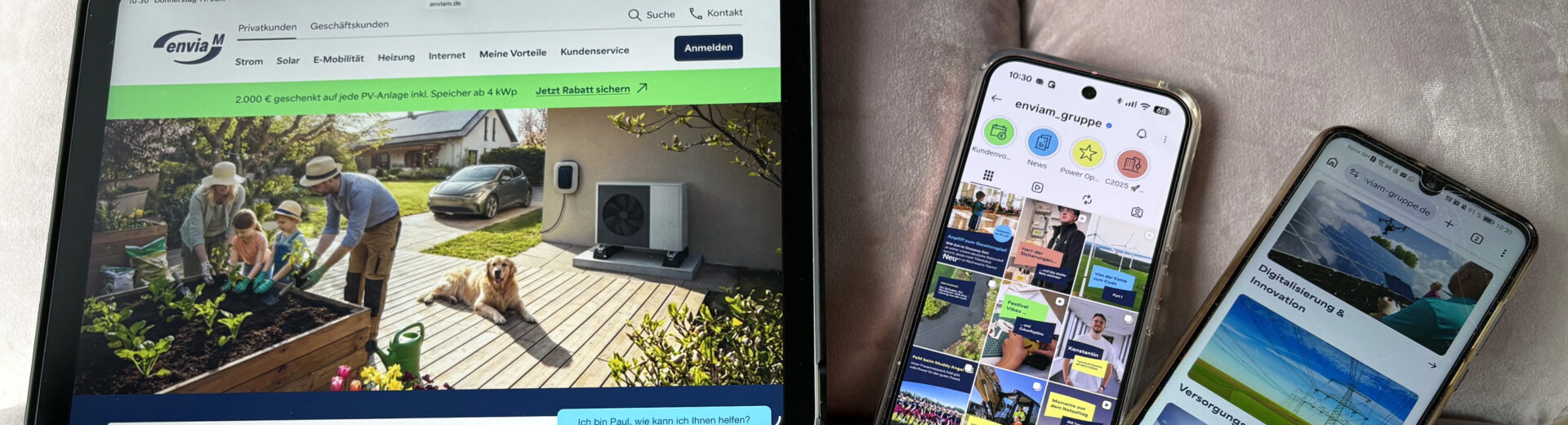 Drei Geräte auf einem Sofa: links ein Tablet mit einer Website über Solar/Heizung (Familie im Garten), daneben zwei Smartphones mit Social-Media- und Info-Seiten.