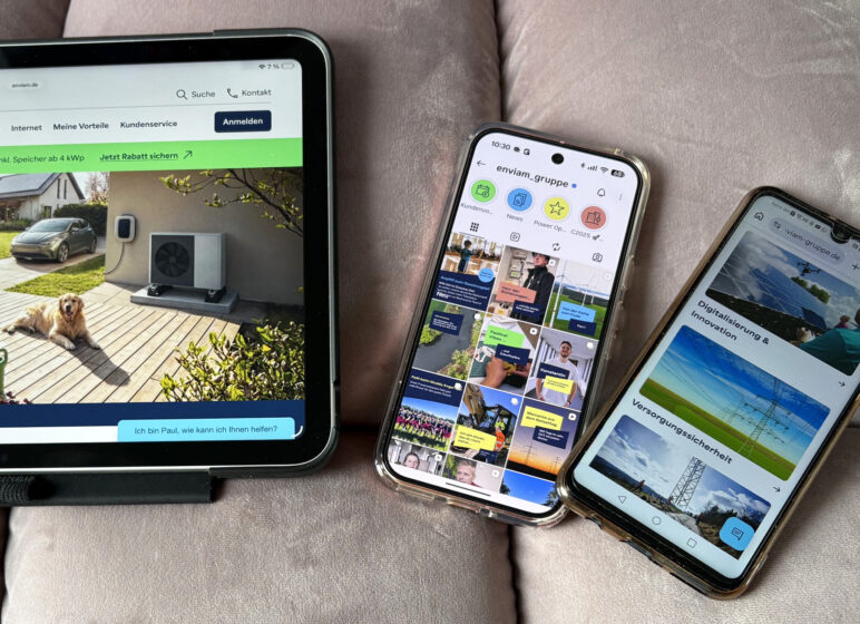 Drei Geräte auf einem Sofa: links ein Tablet mit einer Website über Solar/Heizung (Familie im Garten), daneben zwei Smartphones mit Social-Media- und Info-Seiten.