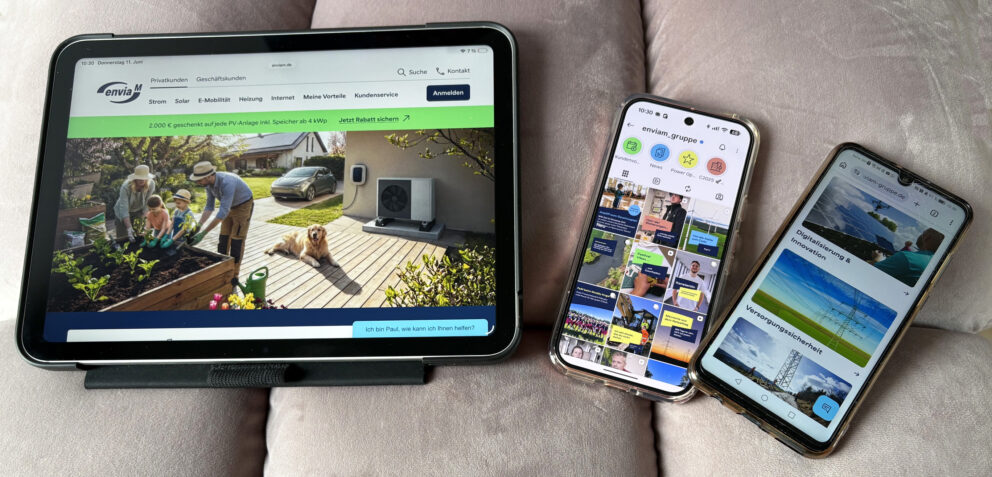 Drei Geräte auf einem Sofa: links ein Tablet mit einer Website über Solar/Heizung (Familie im Garten), daneben zwei Smartphones mit Social-Media- und Info-Seiten.