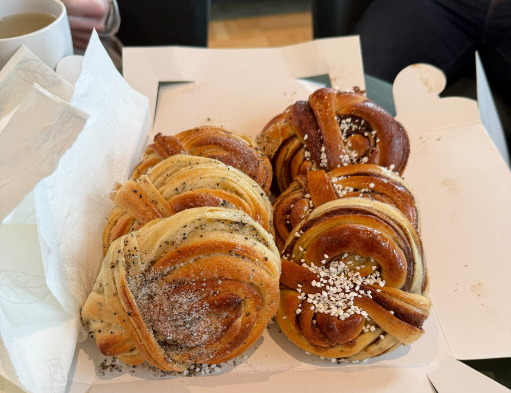 Mehrere frisch gebackene Zimtschnecken mit Zuckerkristallen und Mohn, serviert in einer offenen Pappschachtel neben Papierservietten und einer Tasse.