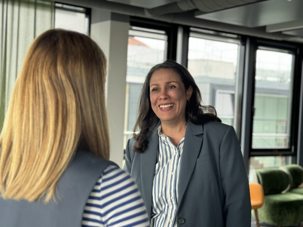 Zwei beruflich gekleidete Frauen in einem modernen Büro, eine lächelt offen der anderen gegenüber.
