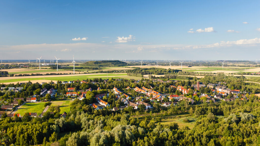 Kleinstadt mit roten Dächern vor weiten Feldern und zahlreichen Windrädern unter blauem Himmel.